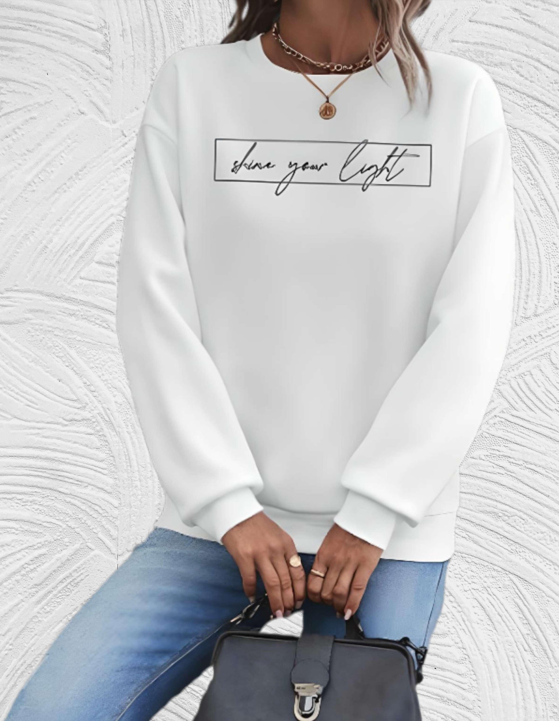 Frau in weißem Sweatshirt mit Schriftzug, blaue Jeans, schwarze Tasche, modisches Outfit.