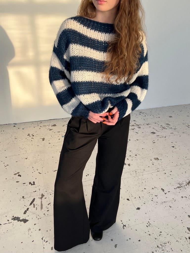 Frau in gestreiftem Pullover und schwarzer Hose, modisch, lässig, Herbstmode, Innenaufnahme.